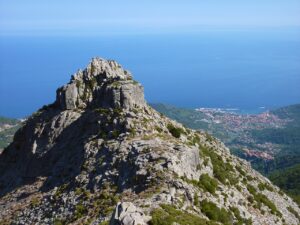 A stunning view from the rugged peak of a mountain on Elba Island, overlooking the blue Mediterranean Sea and the town below. This picturesque scene is perfect for an Elba traveling