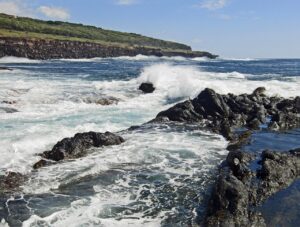 Waves crashing against the volcanic rock formations on Faial Island's coastline, capturing the rugged beauty and dynamic seascape. The scene highlights the island's dramatic shoreline, a key attraction in this Faial travel guide.