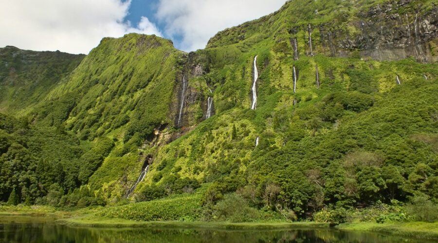 Lush green cliffs of Flores Island with multiple cascading waterfalls, reflecting the island's untouched natural beauty. The verdant landscape is a key highlight in Flores travel guide.