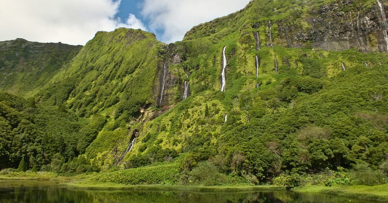 Lush green cliffs of Flores Island with multiple cascading waterfalls, reflecting the island's untouched natural beauty. The verdant landscape is a key highlight in Flores travel guide.