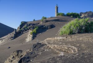 Lighthouse of Ponta dos Capelinhos standing tall against a rugged volcanic landscape, with the ocean in the background under a clear sky