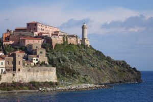 A picturesque view of Portoferraio on Elba Island, featuring historic buildings and a lighthouse perched on a cliff overlooking the blue sea. This scenic spot is a highlight in any Elba travel