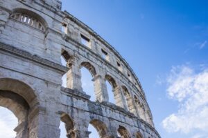 Close-up view of the Pula Arena in Pula, Croatia, showcasing the ancient Roman architecture with its arched walls against a blue sky.