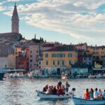 Scenic view of Rovinj, Croatia, showing the town's colorful buildings, waterfront, and boats in the harbor with St. Euphemia's Church tower in the background.