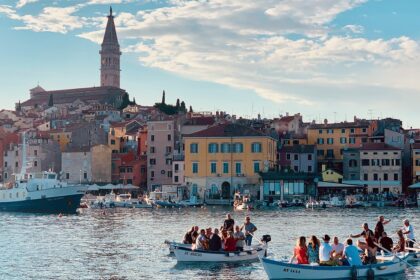 Scenic view of Rovinj, Croatia, showing the town's colorful buildings, waterfront, and boats in the harbor with St. Euphemia's Church tower in the background.