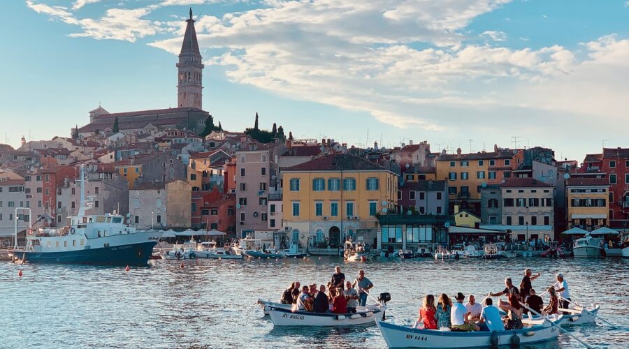 Scenic view of Rovinj, Croatia, showing the town's colorful buildings, waterfront, and boats in the harbor with St. Euphemia's Church tower in the background.