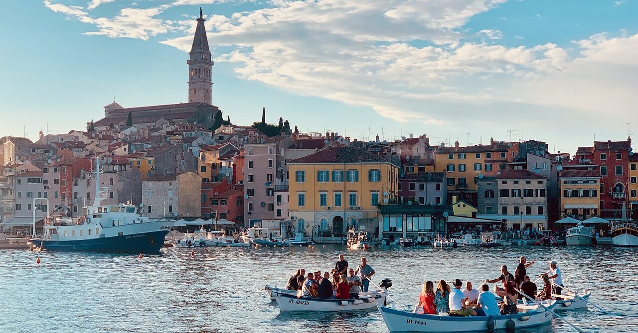 Scenic view of Rovinj, Croatia, showing the town's colorful buildings, waterfront, and boats in the harbor with St. Euphemia's Church tower in the background.