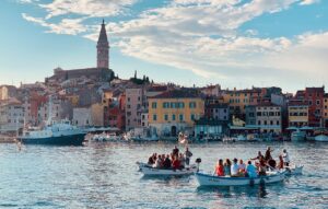 Scenic view of Rovinj, Croatia, showing the town's colorful buildings, waterfront, and boats in the harbor with St. Euphemia's Church tower in the background.