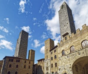 Tall medieval stone towers and historic buildings of San Gimignano under a bright blue sky in Tuscany.