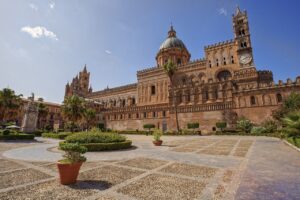 A wide-angle view of Palermo Cathedral in Sicily, showcasing its stunning medieval architecture with a clear blue sky in the background.