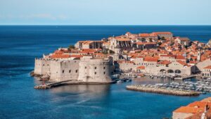Panoramic view of Dubrovnik's old town with its historic city walls, red-tiled rooftops, and harbor along the Adriatic Sea.