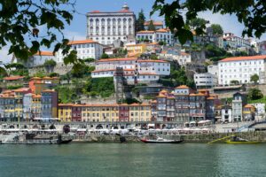 A vibrant hillside view of Porto, Portugal, showcasing colorful buildings stacked along the Douro River with historic architecture and lush greenery.