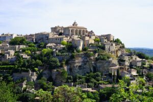 A picturesque view of Gordes, a hilltop village in Provence, France, with its historic stone buildings and lush greenery under a clear sky.