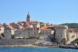 The historic stone buildings of Korčula, Croatia, with their terracotta roofs, seen from the waterfront on a clear, sunny day.