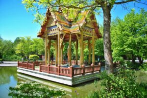 A traditional Thai pavilion in Munich's Westpark, surrounded by lush greenery and reflected in a tranquil pond.