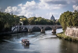 Tourist boat cruising on the Tiber River with the Sant'Angelo Bridge and the dome of St. Peter's Basilica in the background in Rome, Italy.
